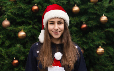 Dreamy Christmas woman. Close up Portrait of woman wearing a santa claus hat with emotion. Against the background of a Christmas tree