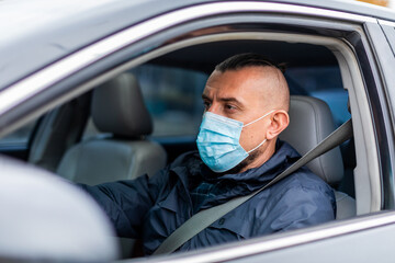 crossing the quarantine zone by car. young man in a medical mask driving a car. Looks ahead