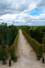 A long hallway in the forest surrounding the Palace of Versailles in France leads off into the distance on a mostly cloudy day.