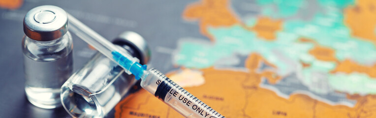 Medical syringe with a needle and a bollte with vaccine on world map.