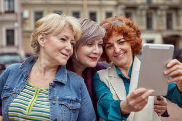 Cheerful and happy old ladies take selfie on tablet PC outdoor.