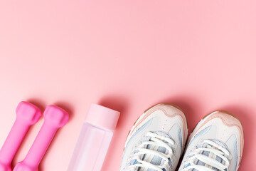 Sneakers, dumbbells on pink background top view, copy space