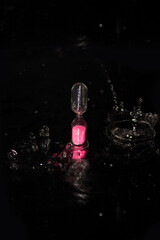 Hourglass with pink sand among splashes on a black background