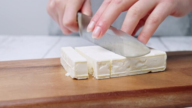 Close-up of Cutting/slicing cubes of feta cheese on a board for a Greek Salad.