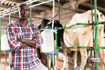 Portrait of farmer man staning near cow milking machines indoor at farm. High quality photo