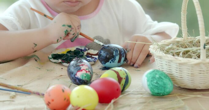 Close up of asian little girl colouring easter eggs with colours and brush on the desk. Preparation of the Easter. Zoom in, slow motion