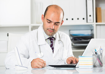 Fototapeta premium Young smiling male working in medical Center at the laptop