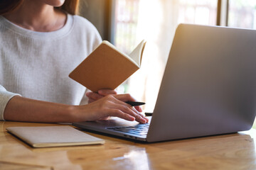 Closeup image of a woman writing on a notebook while working on laptop computer in office