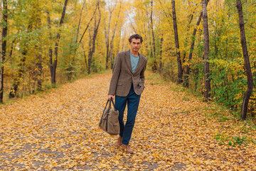 Tall handsome man with a bag on the autumn alley