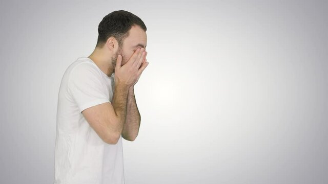 Sleepy male in white t-shirt yawning and rubbing eyes while walking on gradient background.