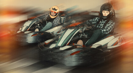 Young positive people in helmets driving racing cars in karting club © JackF