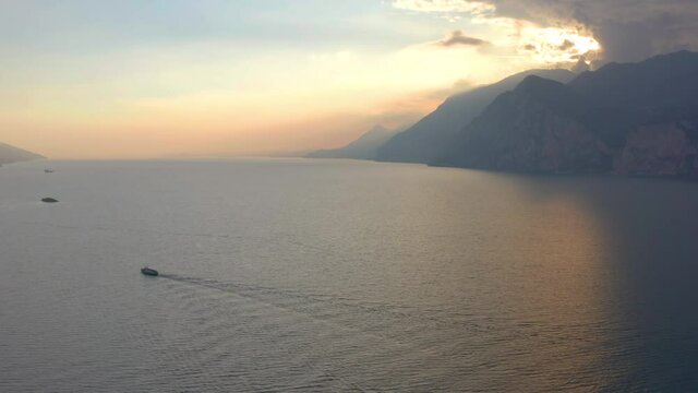 Static, moody, aerial shot of large boat sailing across lake Garda at sunset giving sense of space to the landscape