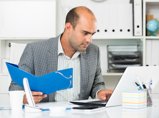 Cheerful man working in the office with folders and files at the laptop