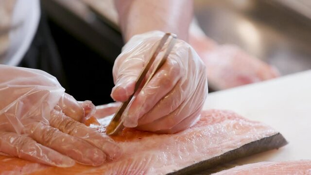 Close up of a chef's hand deboning fresh salmon for a delicious Sushi. Preparing Asian Japanese food in a restaurant kitchen.