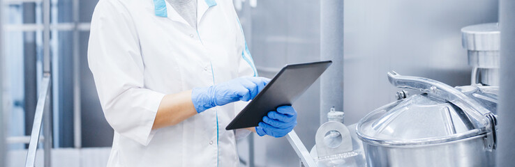 Factory worker inspecting production line tanker in of dairy factory with computer tablet. Concept food industry banner