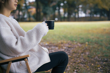 森でホーローカップを持ちイスに座り休憩する女性