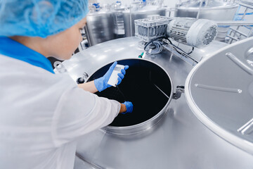 Dairy production, operator woman engineer checks temperature of steel tank with milk. Industrial...