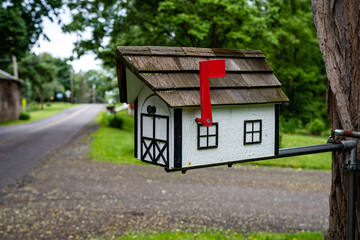 a traditional American wooden mailbox that looks like a cottage, on the side of a village road