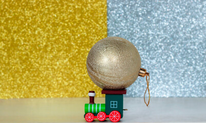 Toy wooden locomotive carries a large Christmas tree toy close-up. Christmas card for winter holidays. Brilliant defocused background. Free space for copying.