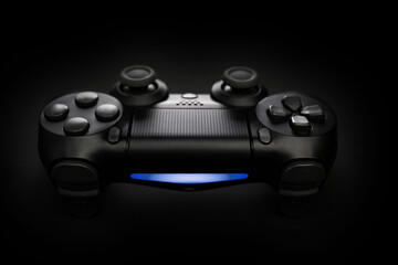 Closeup photo of video game console gamepad joystick controller on black background with blue light.