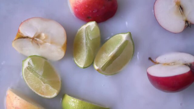 Sliced fresh lemon falling into milky water decorated with fresh apples. Organic Fruit is dropped into white liquid with splashes. Filmed in Prores.