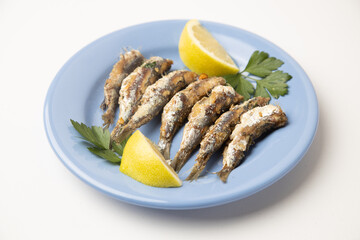 fried sardines, in blue plate with lemon wedge