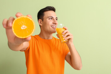 Handsome man with ripe orange and juice on color background