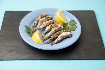 fried sardines, in blue plate with lemon wedge