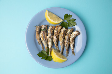 fried sardines, in blue plate with lemon wedge