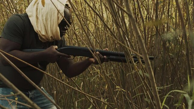 Afro-American sneaking in forest with man pump action shotgun.