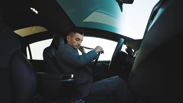 Handsome young man pinches seat belt and riding happily smiling. Joyfull driver. Lifestyle, road, car, driver concept. Protection of a person in vehicles. Road safety regulations concept.