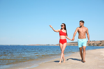 Fototapeta premium Woman in bikini and her boyfriend on beach, space for text. Happy couple