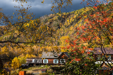 Dramatic stormy sky in the mountains. Picturesque autumn landscape with colorful vivid forest and country houses.