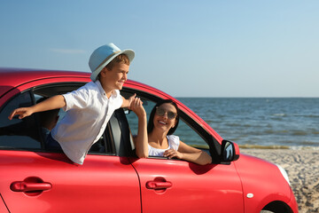 Happy woman and her son in car near sea. Summer trip