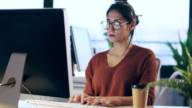Shot of beautiful young business woman working with computer while talking with earphone sitting in the office.