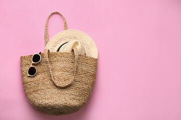 Elegant woman's straw bag with hat and sunglasses on pink background, top view. Space for text