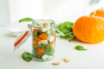 Bright autumn salad of pumpkin, spinach and feta in a jar. A good snack on the road. Salad and ingredients on a light background. 