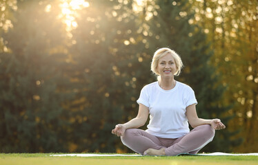 Mature woman practicing yoga on green grass in park