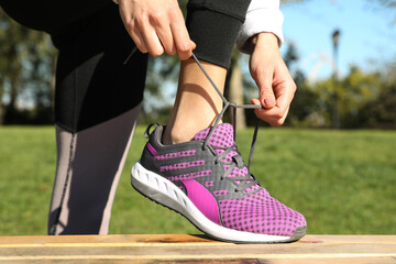 Sporty woman tying shoelaces in park on sunny morning, closeup