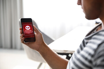 Man holding smartphone with warning about virus attack at home, closeup