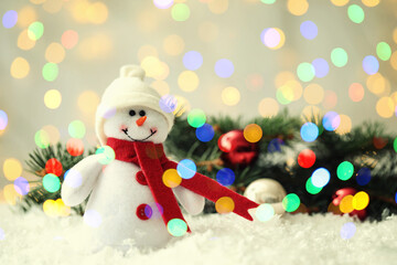 Cute snowman and fir tree branches with Christmas balls on snow, bokeh effect. Space for text