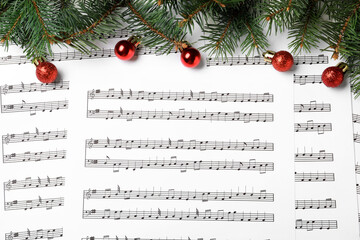 Fir tree branches and red balls on Christmas music sheets with notes, flat lay