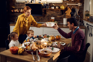 Happy parents with kids enjoying in Thanksgiving dinner in dining room.