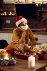 Pensive woman with face mask sitting alone at dining table on Christmas.