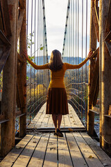 Fototapeta na wymiar a young woman stands with her back to the old suspension bridge
