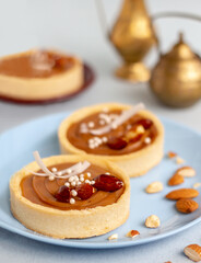nougat or caramel filling tartlets with nuts (whole almond) on blue plate, pair of french cakes,...