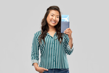 Naklejka premium travel, tourism and vacation concept - happy smiling young asian woman with air ticket and passport over grey background