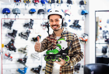 Smiling satisfied pleasant guy deciding on new roller-skates in sports store