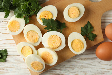 Board with boiled eggs on white wooden background