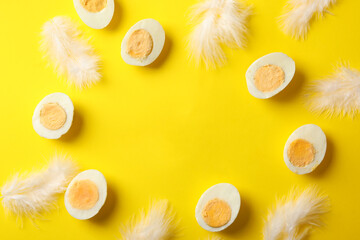 Boiled eggs and feathers on yellow background, top view